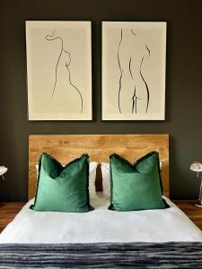 Una cama con dos almohadas verdes y dos cuadros. en 'Just Beachy' Muizenberg Beach Apartment, en Muizenberg