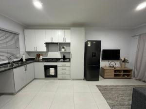 une cuisine avec un réfrigérateur noir et des armoires blanches dans l'établissement Sarona Habitat Urban Escape 1 Bedroom Apartment, à Gaborone