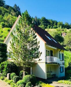 a white house with a balcony and a tree at Ferienhaus Oesterle - Idyllisches Schwarzwaldhaus am Bach mit Terrasse & Balkon in Schönmünzach