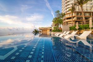 a swimming pool with white chairs and a building at Apec Mandala Wyndham Mui Ne Ngoc Linh in Mui Ne