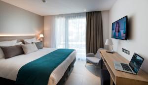 a hotel room with a bed and a desk with a laptop at Golden Tulip Sophia Antipolis - Hotel & Spa in Valbonne
