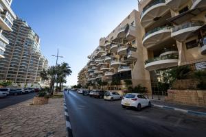 a street with cars parked next to tall buildings at Sea Suites - סוויטות מהממות עם מרפסת ליד המרינה באשקלון in Ashqelon