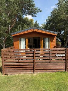 a small cabin with a wooden fence in the grass at Happy Ever After Lodge in Morpeth