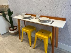 a table with two yellow stools and a table with plates and cups at Studio XV Centro Florianópolis Centro Sul Eventos in Florianópolis