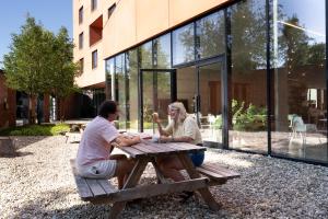 two women sitting at a picnic table in front of a building at Hostel Groeninghe in Kortrijk