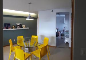 a dining room with a glass table and yellow chairs at Apartamento na Ponta Verde in Maceió