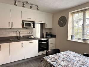 MAYS COTTAGE - Blakeney في بلايكيني: مطبخ فيه دواليب بيضاء وطاولة وساعة