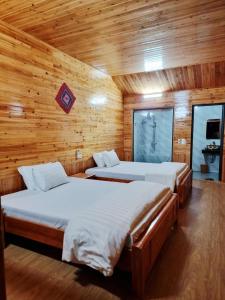 two beds in a room with wooden walls at Quyen Homestay in Bắc Hà