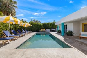 a pool with chairs and umbrellas next to a house at The Ricardo! Mid-Century Villa with Saltwater Pool in Palm Springs
