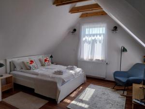 a white bedroom with a bed and a blue chair at Papoula Vendégház - Köveskál in Köveskál