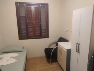 a small room with a bed and a chair and a window at Hospedagem Joinville in Joinville +1 photo