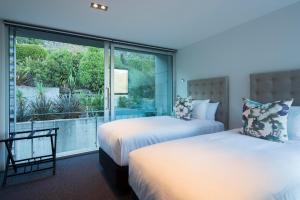 two beds in a room with a large window at Villa De Luxe, a Relax it's Done luxury holiday home in Queenstown