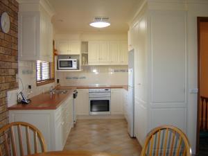 uma cozinha com armários brancos e uma mesa e cadeiras em Dalmeny Shores em Dalmeny