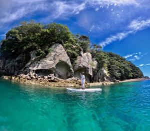 Un hombre parado en una tabla de remo en el agua cerca de una isla en シーラニ白浜荘, en Kannoura