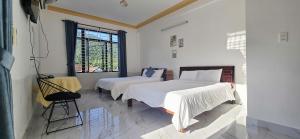 a white bedroom with two beds and a window at Hùng Cúc homestay in Tân Hiệp