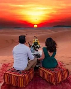 a man and woman sitting in the desert watching the sunset at Bivouac Camel Trips in Merzouga +64 photos