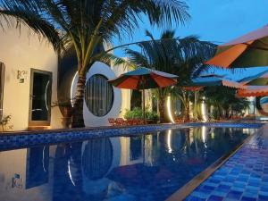 a swimming pool with umbrellas and palm trees next to a building at paparazzi homestay in Xuyên Mộc +56 photos