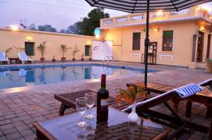 a table with wine glasses and an umbrella next to a pool at Koolwal Kothi Zinc Journey by The Fern, Nawalgarh, Rajasthan in Nawalgarh