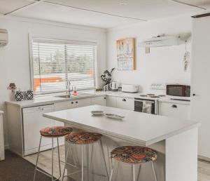 a white kitchen with a counter and stools in it at Hamptons in Lancelin