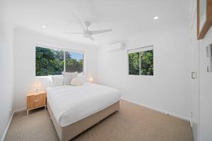 a white bedroom with a bed and two windows at The Palms in Coolum Beach - Unit A in Coolum Beach
