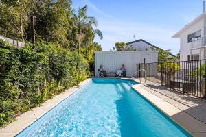 two people sitting next to a swimming pool in a house at The Palms in Coolum Beach - Unit B in Coolum Beach