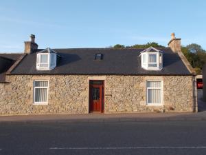 een stenen gebouw met een rode deur en twee ramen bij Inveravon Holiday Home in Dufftown