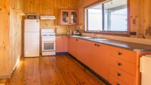cocina con armarios naranjas y nevera blanca en The Lake Cabin, en Lake Tabourie