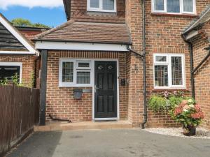 ein Backsteinhaus mit schwarzer Tür und Blumen in der Unterkunft Sunnyfield Cottage in Coulsdon