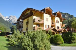 Un edificio en las montañas con arbustos delante. en Residence Alpenrose, en Molveno