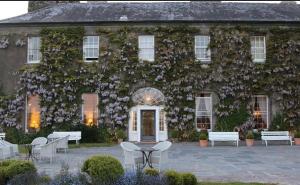 a building covered in ivy with tables and chairs at Eastbury House near Garryvoe Hotel & Ballymaloe House in Cork