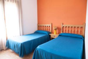 two beds in a room with blue sheets and a window at La Cabaña in Caspe