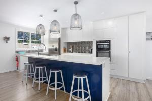 BundeenaにあるDiscover Lambeth Walk Beach Homeの白いキャビネットとバースツール付きの青い島のあるキッチンが備わります。