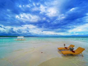 zwei Stühle an einem Strand mit einem Boot im Wasser in der Unterkunft Amorita Resort Palawan in Puerto Princesa