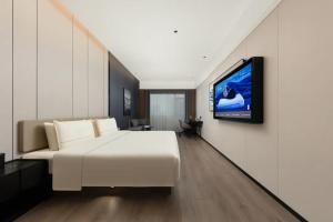 Atour Hotel Hohhot Hailiang Plaza Zhongshan Road Subway Station في هوهوت: غرفة نوم بسرير ابيض وتلفزيون على جدار