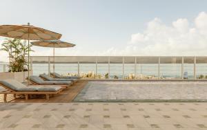 a pool with chairs and umbrellas next to the ocean at Fanaya Hotel Jeddah by Brassbell فندق فنايا جدة in Jeddah