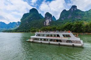 a boat on the water with mountains in the background at Guilin Qingshanshe Hotel -Free pick up train station stay two nights in Guilin