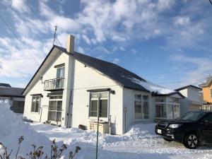 a white house with a car parked in the snow at Guest House Hagoromo 39 - Vacation STAY 12003v in Kiyosato