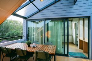 a glass extension of a house with a wooden table and chairs at Tabebuia House ทาเบบูย่าเฮ้าส์ in Pathiu