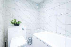 a white tiled bathroom with a toilet and a plant at Sunrise Haven Sleeps 7 with Parking in Gravesend