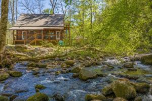 a log cabin in the woods next to a stream at Tridents Creek by American Patriot Getaways in Rocky Grove