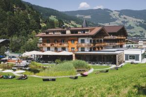 a large building in a field with people sitting at Ski & Bike Hotel Wiesenegg in Saalbach-Hinterglemm