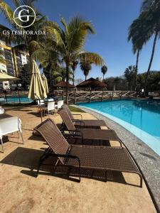 un groupe de chaises et de parasols à côté d'une piscine dans l'établissement Le jardin Caldas Novas, à Caldas Novas
