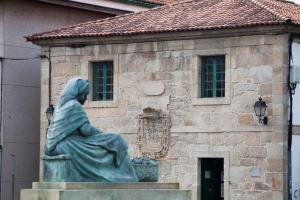 una estatua de una mujer sentada frente a un edificio en Nido PADRON, en Padrón