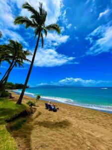 people sitting under a palm tree on a beach at Maui Makai Condo - Completely renovated 1 bedroom 1 bath condo, just steps away from Kahana Beach in Kahana