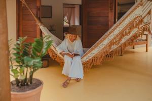 una mujer sentada en una hamaca leyendo un libro en Chalé Refúgio da Mata em Trancoso, en Trancoso