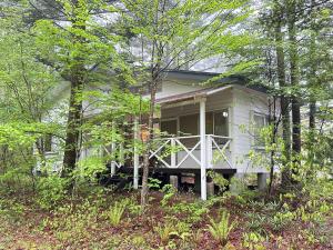 a white house with a porch in the woods at Summer Cool Forest Cottage-北軽井沢 夏涼の森コテージ- in Tsumagoi