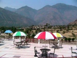 a patio with tables and umbrellas with mountains in the background at Mashoo Resort in Shamshi