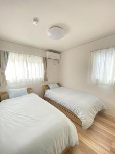 two beds in a room with white sheets and windows at Shonan Katase HOME - Vacation STAY 12525v in Fujisawa