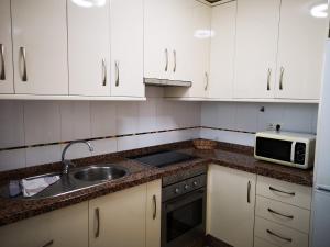 a kitchen with white cabinets and a sink and a microwave at Terrasol Torrelitoral 1 dormitorio in Torre del Mar