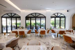 ein Esszimmer mit weißen Tischen und Stühlen und Fenstern in der Unterkunft Chimaera Hotel in Himarë